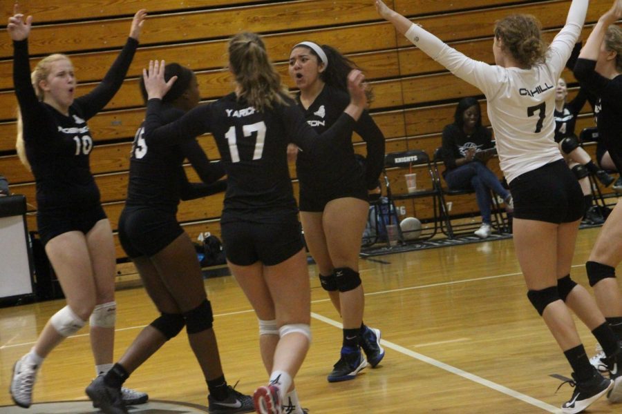 The Lady Knights celebrate as Lauren Johnson (19) serves up an ace.