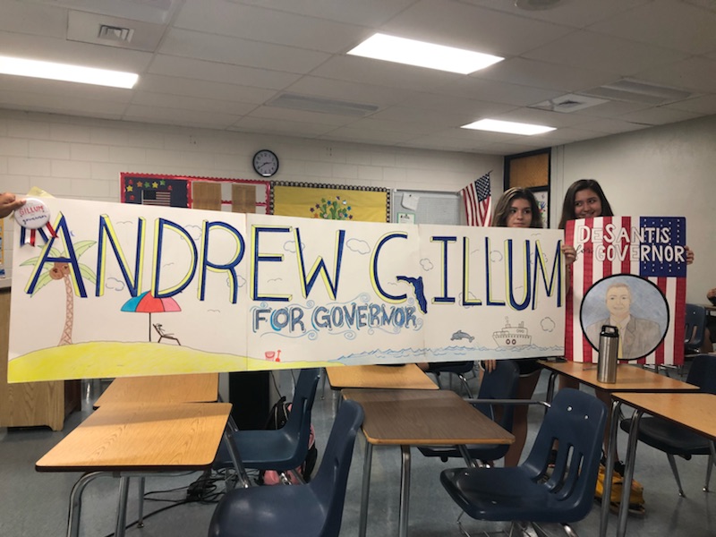 Three students display the political posters they made for their chosen candidate. 