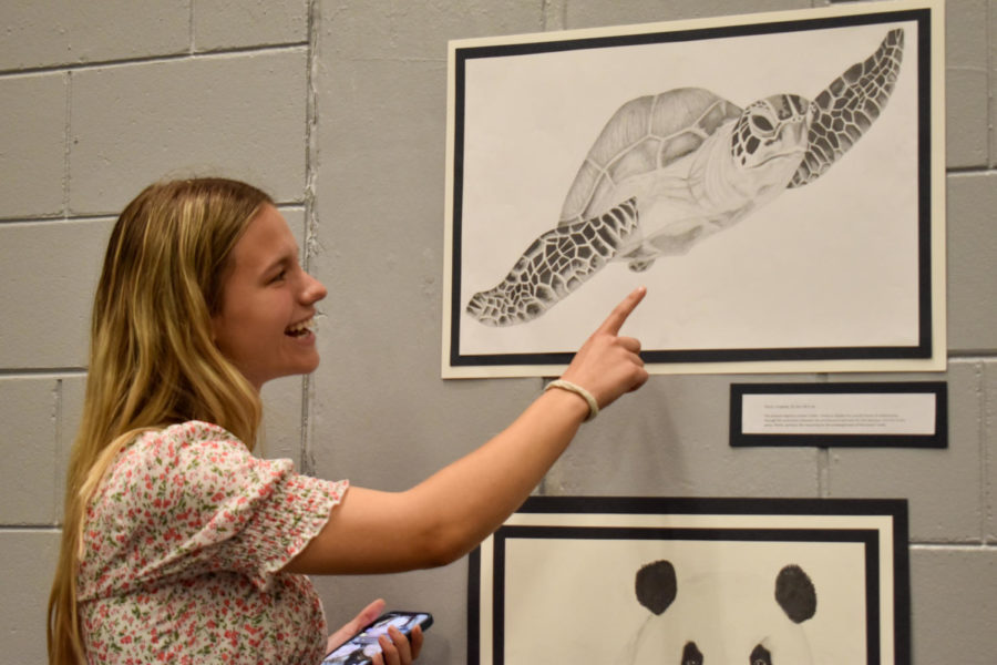 Cassidy Lund (22) points to her graphite drawing of a sea turtle. The piece is titled Plastic, referring to the cause of sea turtle endangerment. Lunds theme for her portfolio was endangered species, with many being specific to Florida. 
