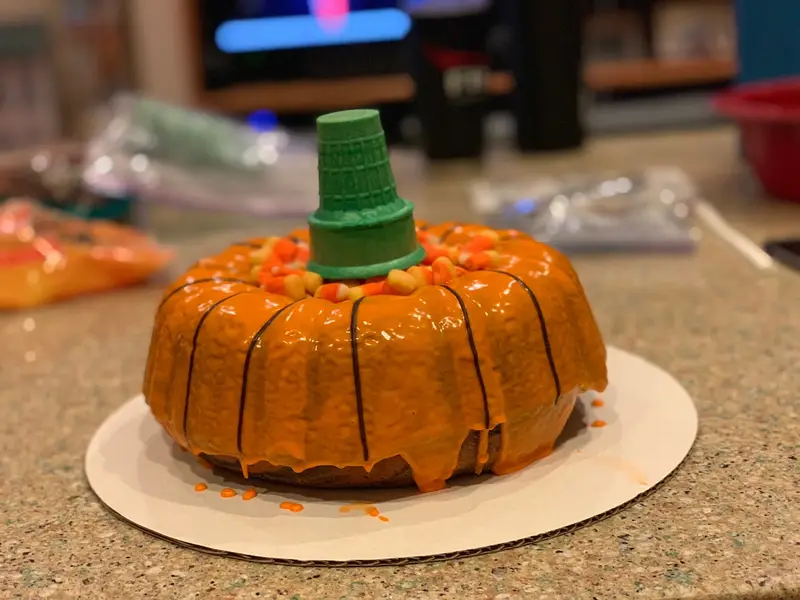 A delicious Halloween Bundt Cake topped with candy corn, a green sugar cone, and orange glaze.