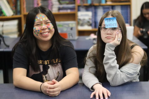 Cecilia Cheng (24) smiles while Keirra McGoldrick (24) frowns as they model the differences between how IB and traditional students feel in school. Chengs face is covered in stars and A+ stickers while McGoldrick only has a sticky note that says TRY HARDER.