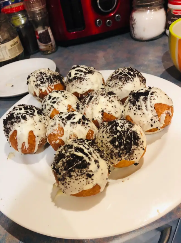 Delicious cookies and cream stuffed doughnuts topped with white chocolate and crumbled Oreo pieces.

