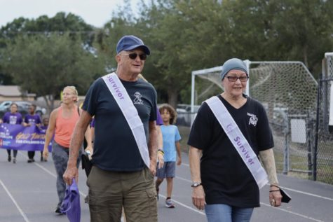 Cancer survivors take a celebratory walk around the track as volunteers and students cheer them on from the field.