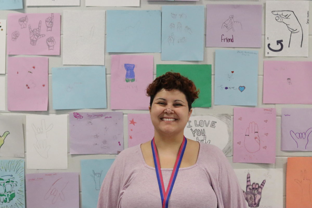 New ASL teacher, Jessie Dorsey, standing in front of a wall plastered with drawings of different ASL words. 
