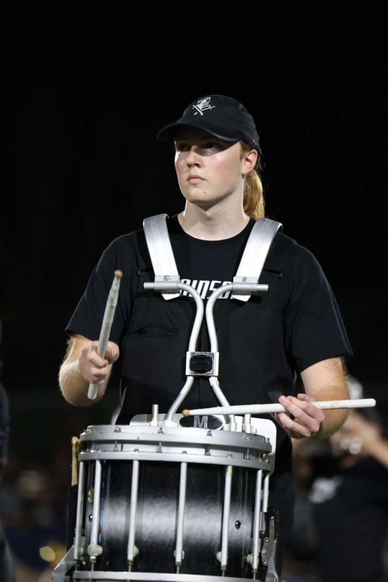 Andrew Bartholomay ('25) stands concentrated on the field playing his drums. 