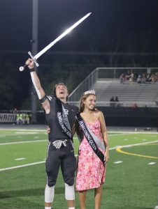 Xander Logan (‘25) and Laurie Launikitis stand side by side after being crowned Homecoming King and Queen while Logan holds the sword high in the sky. 