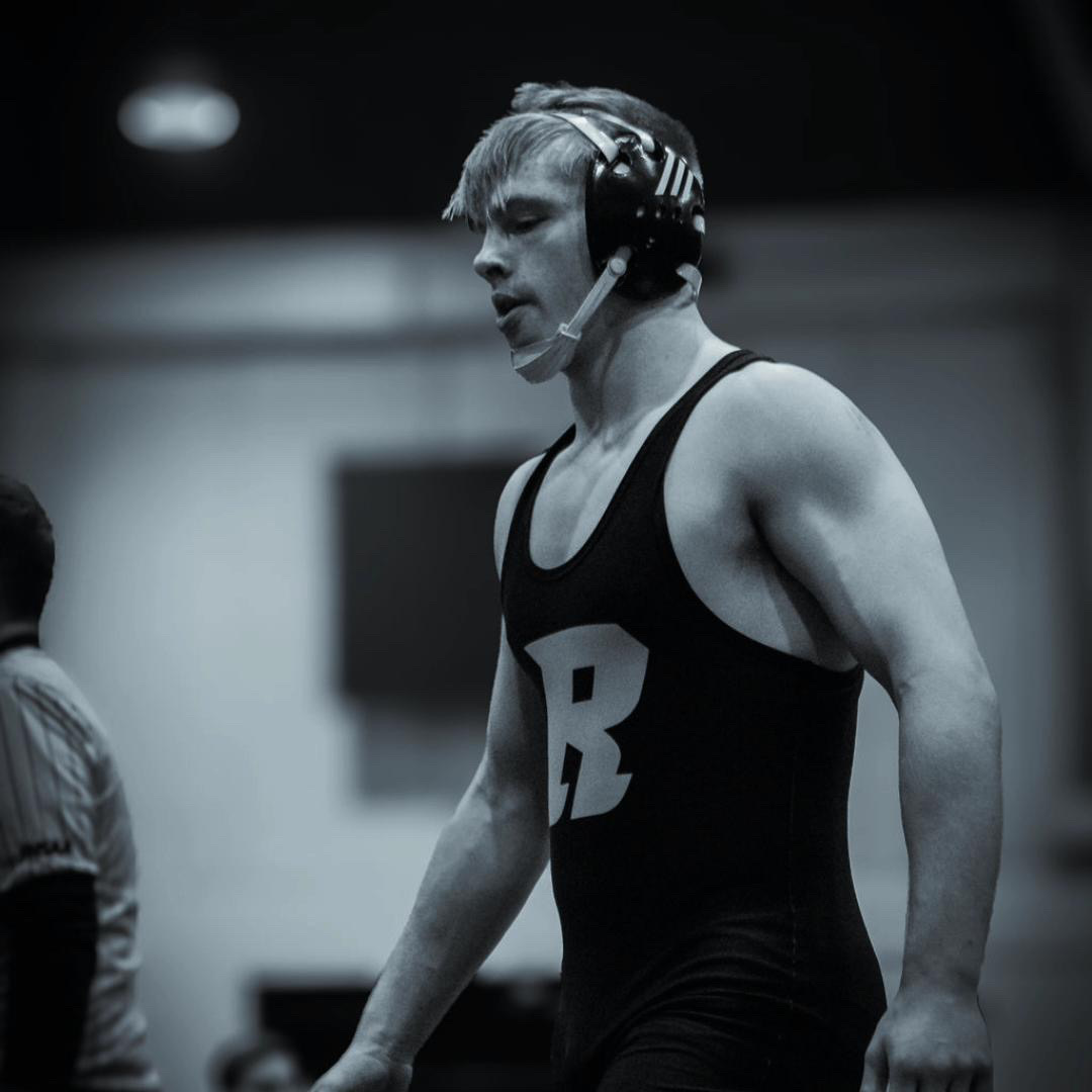 Arron McCarty stands at a wrestling match in his Robinson uniform and gear ready to wrestle. 